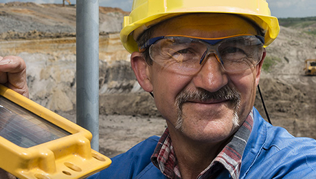 Ein Bergarbeiter mit gelbem Helm und Schutzbrille lächelt und bedient ein technischen Gerät