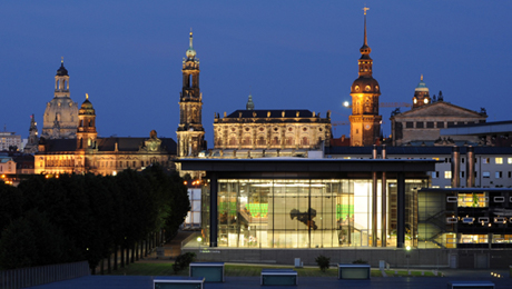 Der abendliche und von innen beleuchtete Glasbau des Sächsischen Landtags, im Hintergrund die Altstadt von Dresden