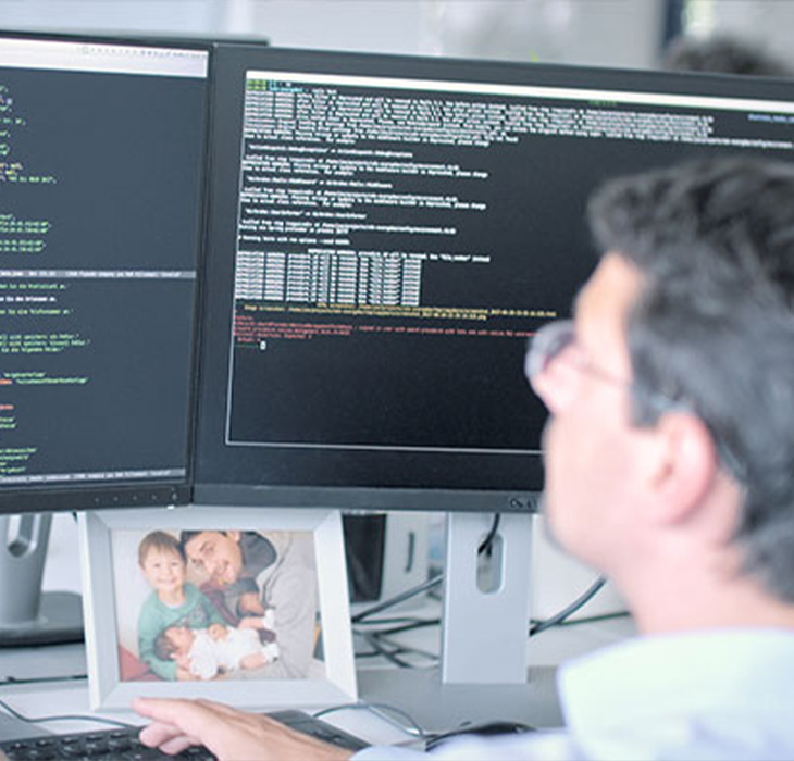 Blick über die Schulter eines Entwicklers von webit! auf zwei Bildschirme mit Quelltexten in verschiedenen Farben.