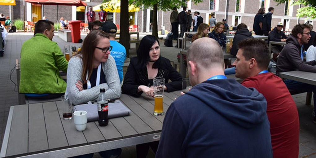 Zwei Mitarbeiterinnen von webit! sind auf den TYPO3 Developer Days 2018 in Düsseldorf. Sie sitzen an einem Tisch und sprechen mit zwei Männern.