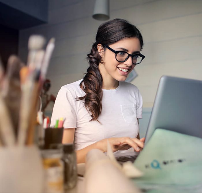Eine junge Frau arbeitet am Laptop und lächelt.