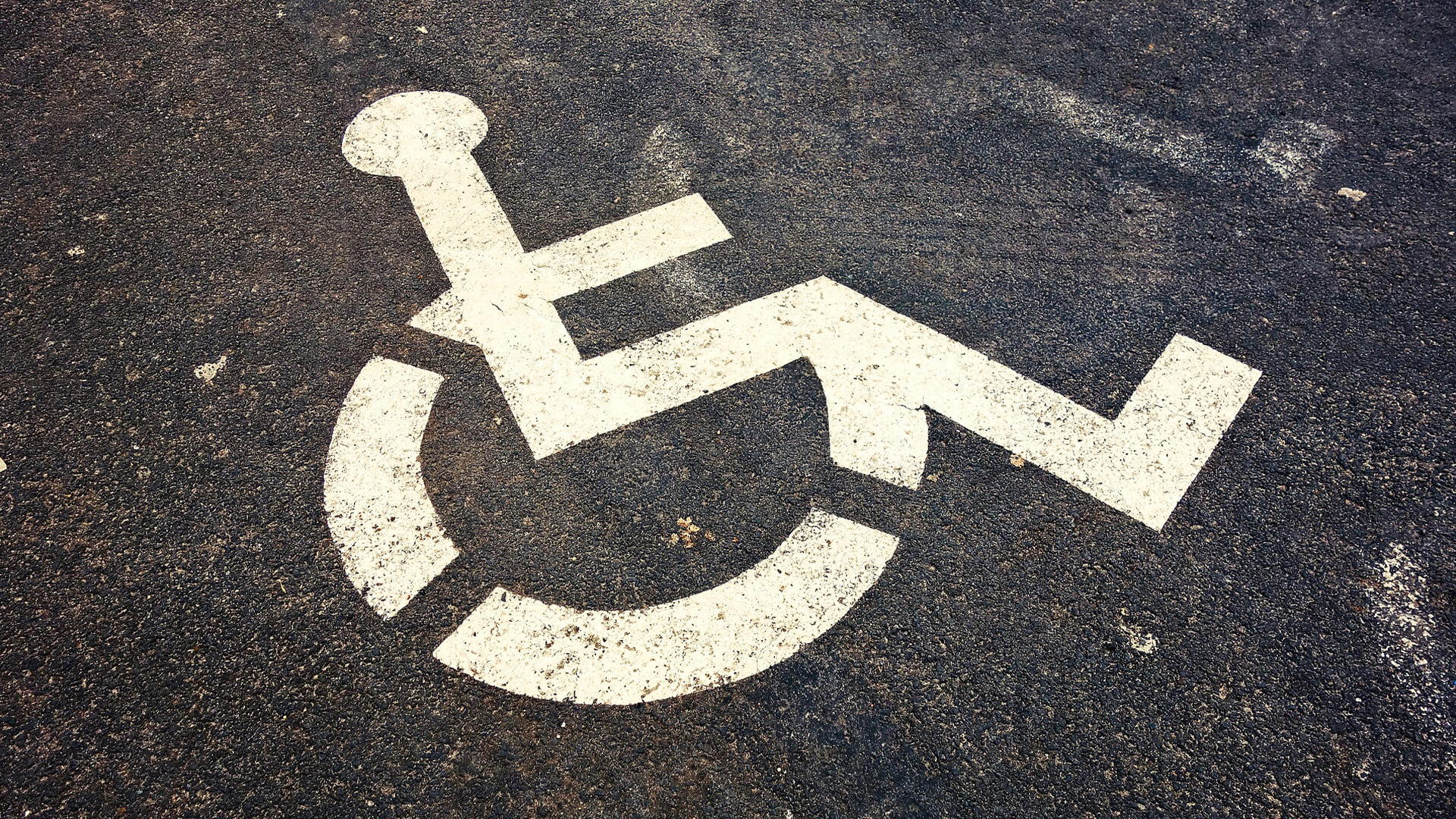 Symbol eines Rollstuhlfahrers in weiß auf Asphalt.
