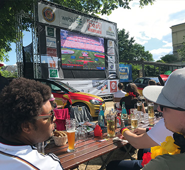 Blick über die Schulter zweier Männer, die im Biergarten einem Fußballspiel folgen