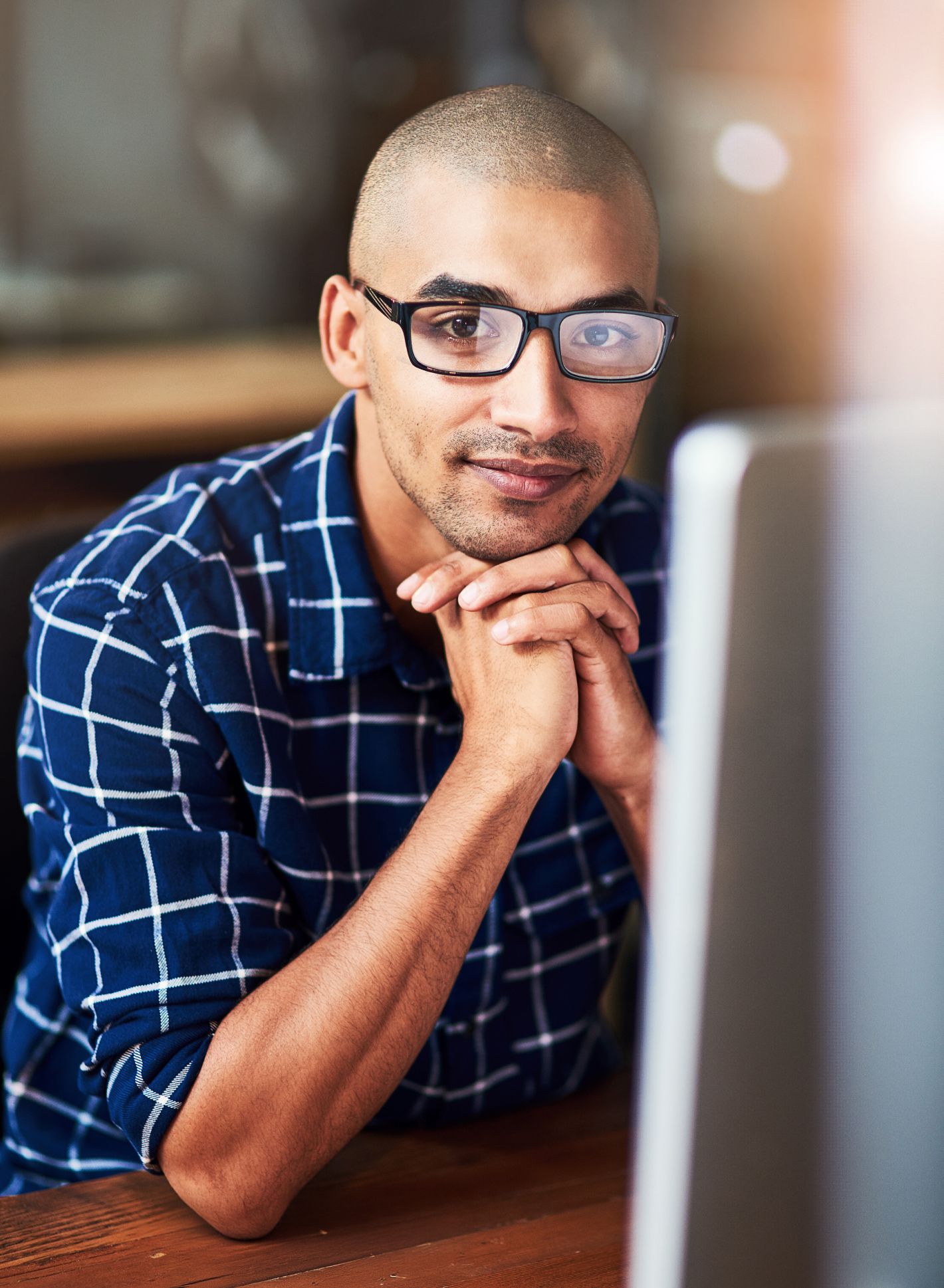 Eine Person mit Brille und kariertem Hemd stützt das Kinn auf gefaltete Hände und blickt nachdenklich auf einen Computerbildschirm.