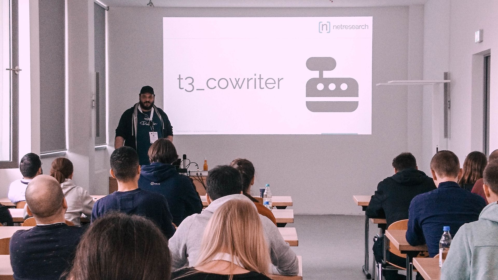 Eine Person präsentiert „t3_cowriter“ auf einer Projektionsleinwand vor einem Publikum.