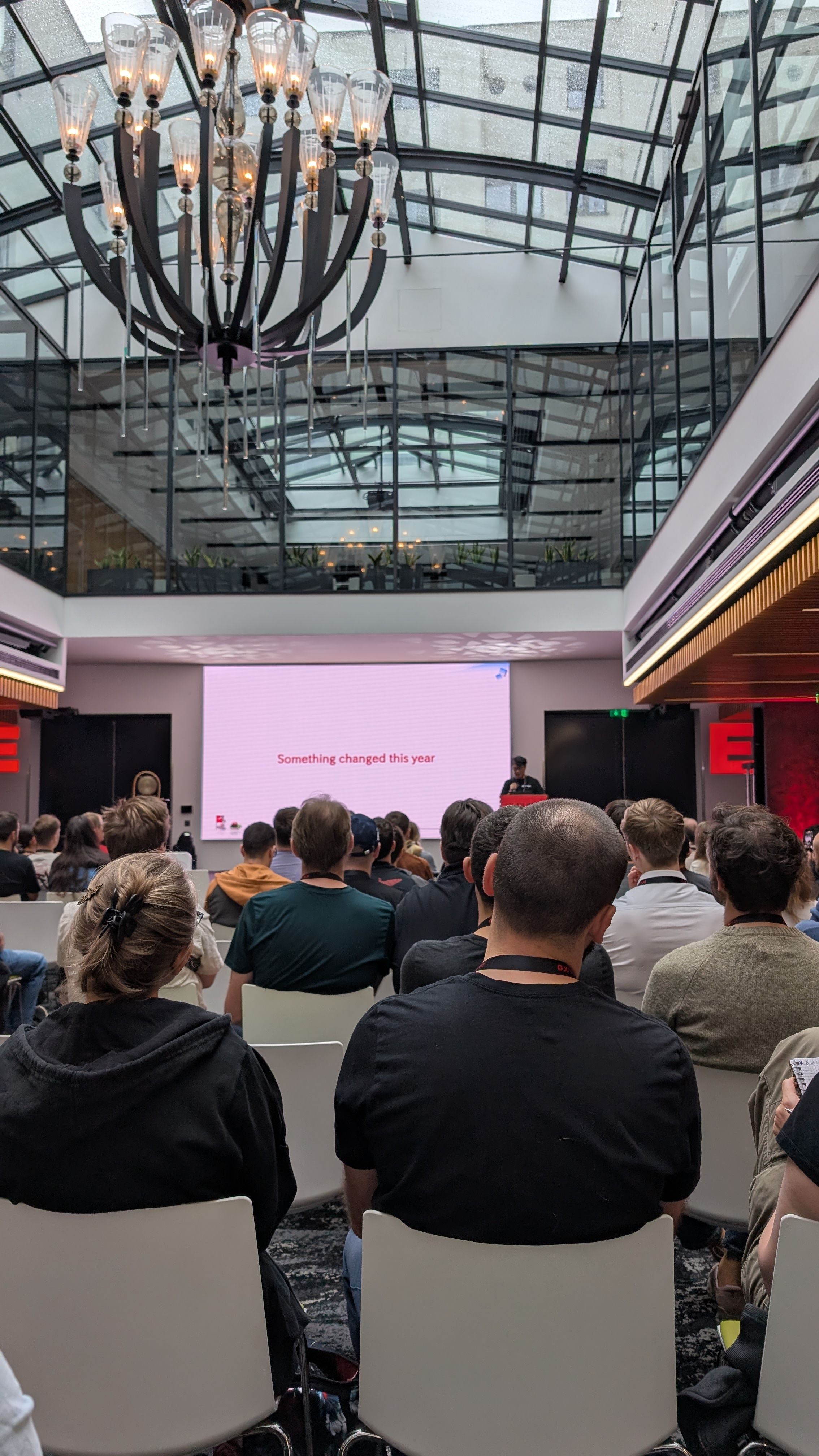Menschen saßen in einem Konferenzraum und hören einem Sprecher vor einem Bildschirm zu, auf dem stand: "Dieses Jahr hat sich etwas verändert."