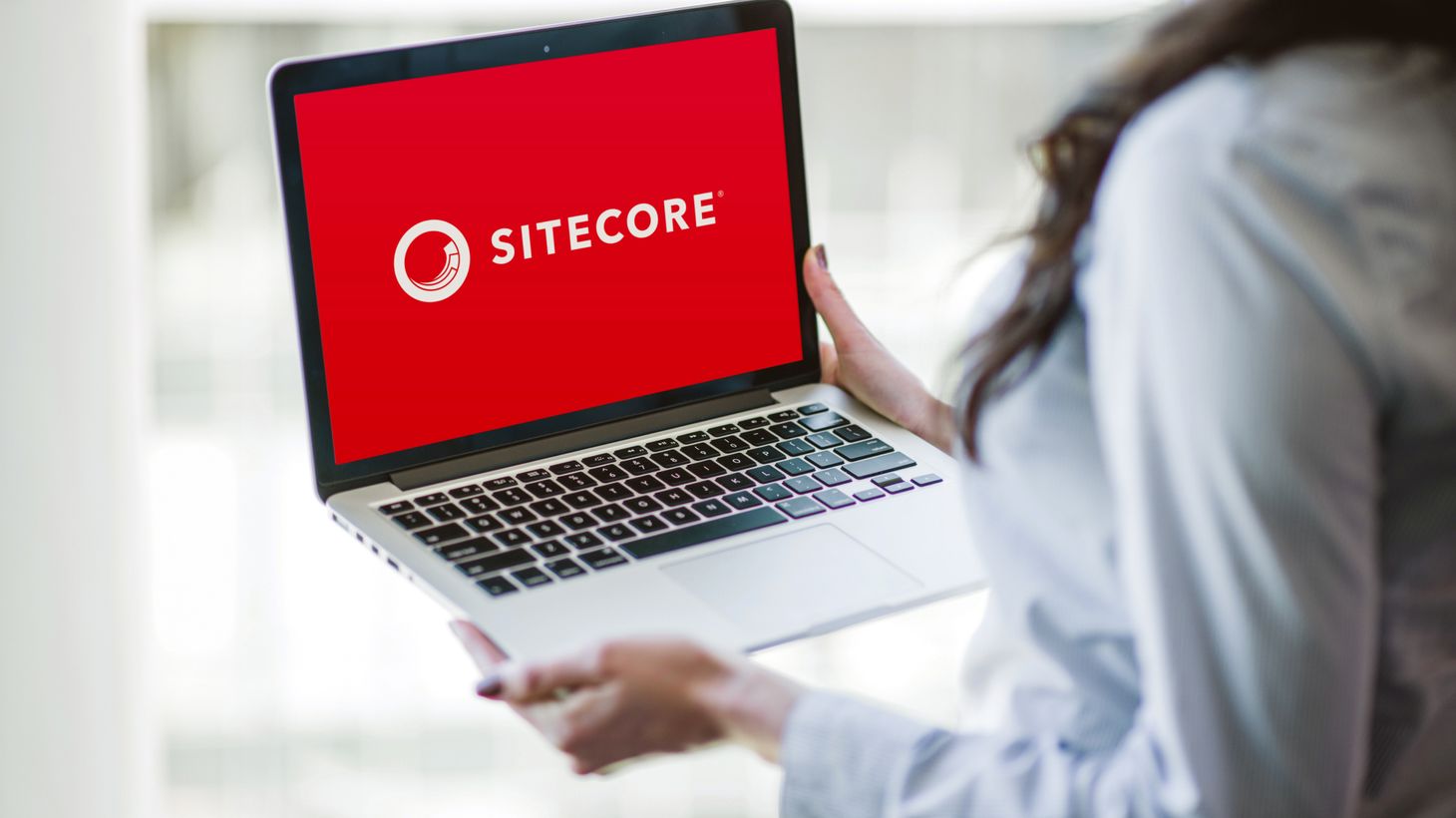 ChatGPT: Eine Person hält einen Laptop, auf dessen rotem Bildschirm das Sitecore-Logo zu sehen ist.