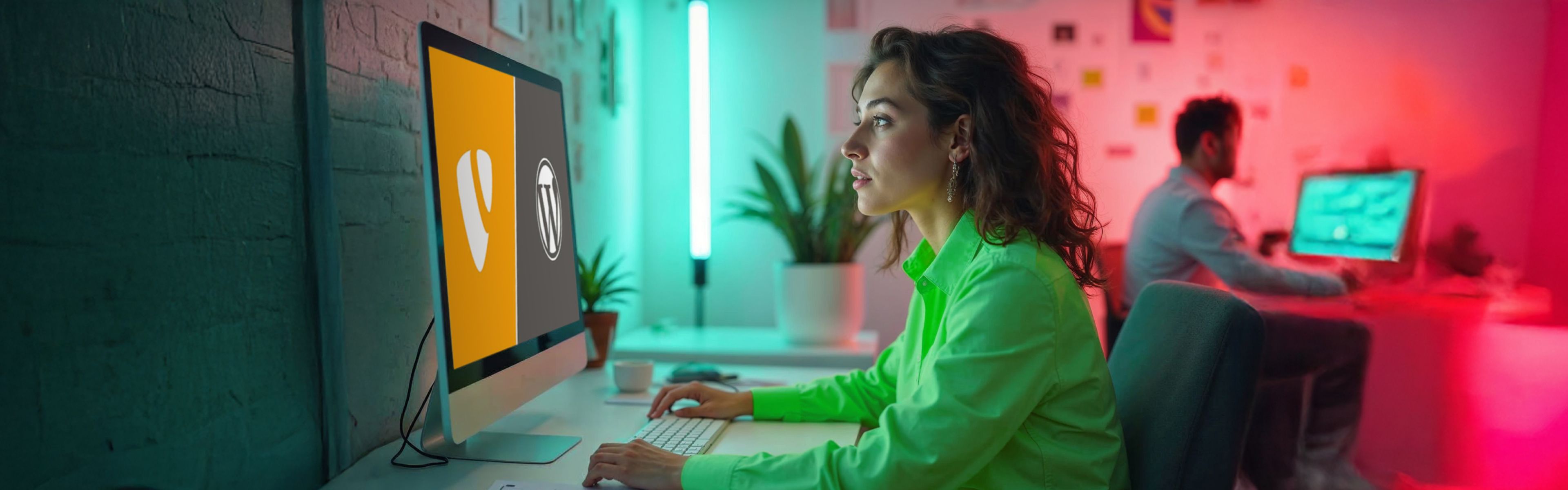 Eine junge Frau sitzt konzentriert an einem Schreibtisch und arbeitet an einem Desktop-Computer. Auf dem Bildschirm sind die Logos von TYPO3 und WordPress zu sehen, die nebeneinander angezeigt werden. Der Raum ist in moderne, farbenfrohe Beleuchtung getaucht – mit einem Mix aus Grün-, Rot- und Blautönen. Im Hintergrund arbeitet ein Mann an einem weiteren Computer. Die Umgebung wirkt kreativ und technisch zugleich.