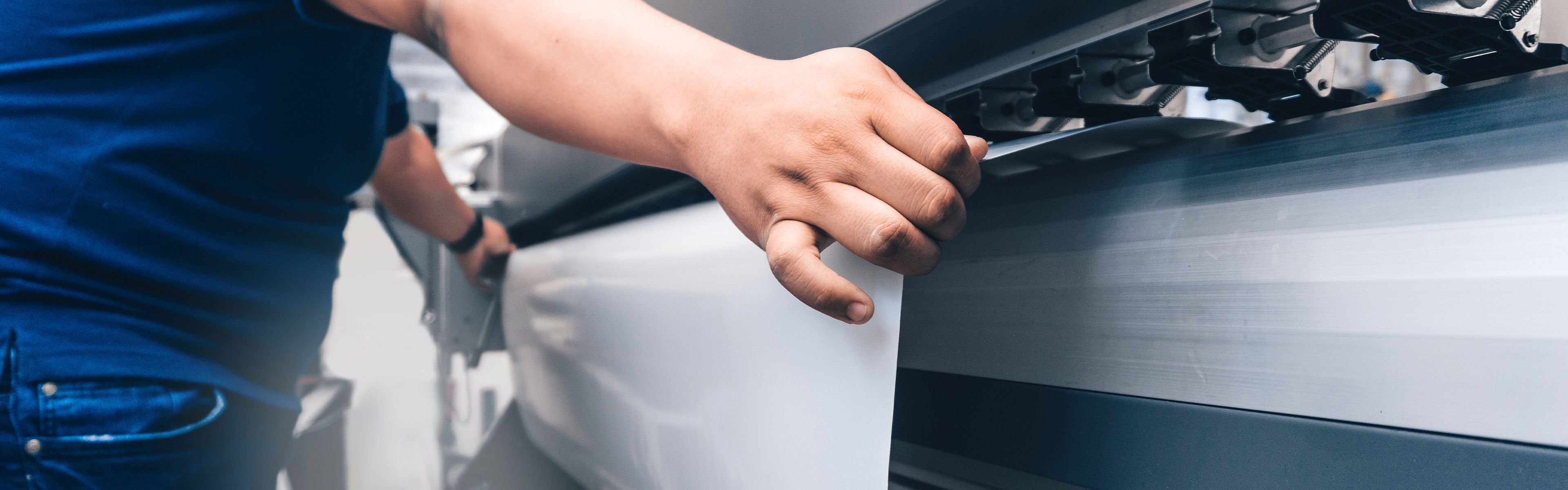 Eine Person bedient einen großen Industriedrucker und justiert weißes Material, das in die Maschine eingelegt wird.