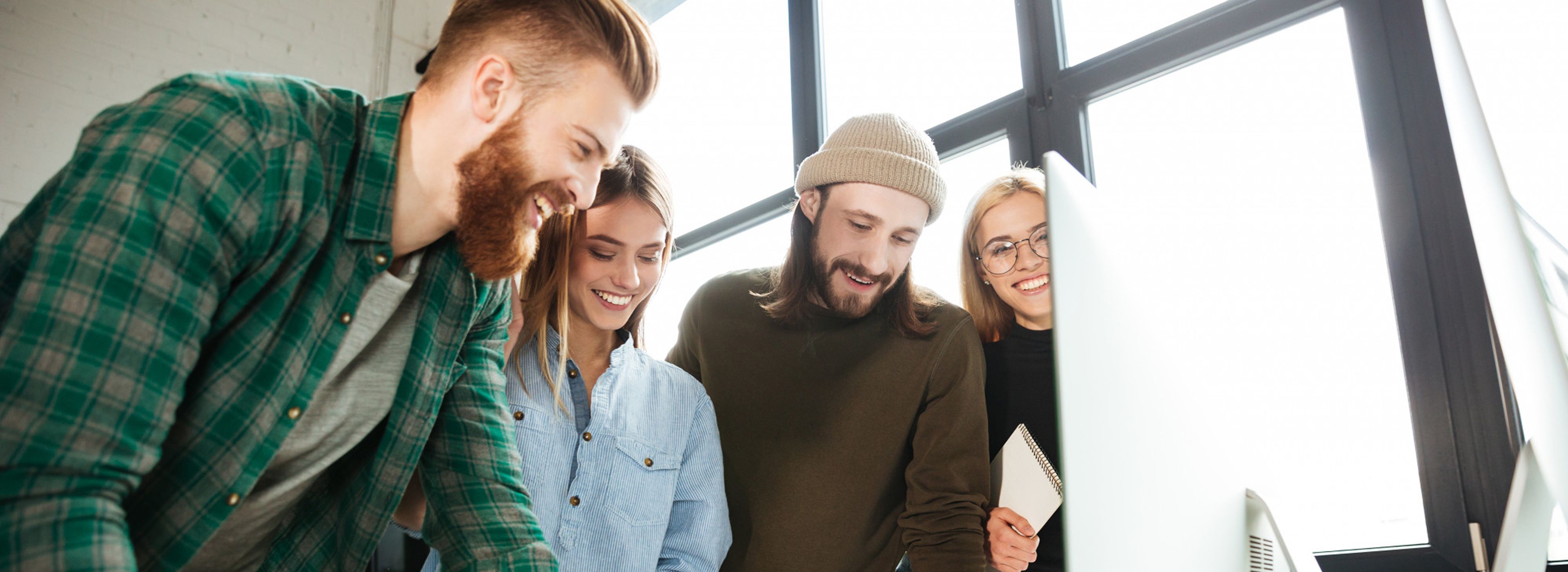 Eine Gruppe von vier Personen lächelt und schaut auf einen Computerbildschirm in einem hellen Büro.