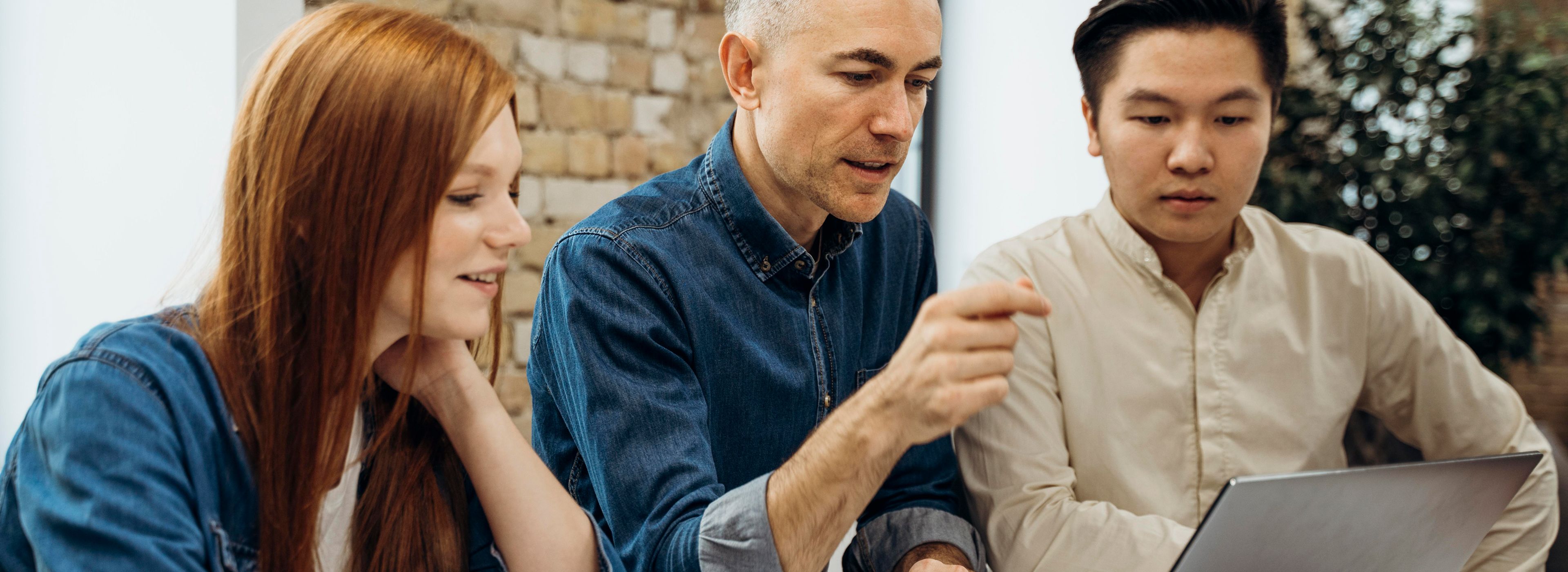 Drei Personen sitzen an einem Tisch und konzentrieren sich auf den Bildschirm eines Laptops.
