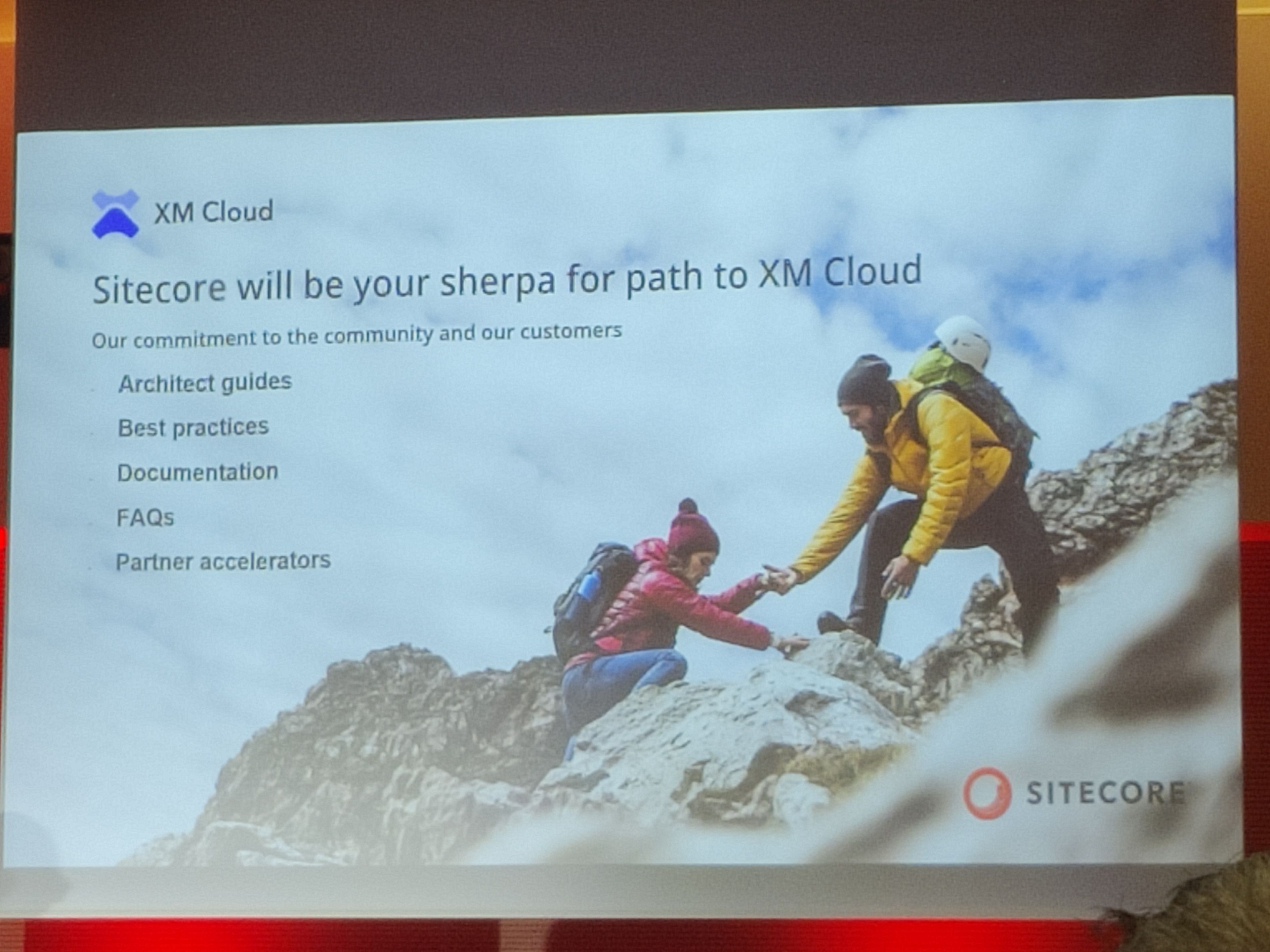 Eine Präsentationsfolie zeigt den Titel „Sitecore will be your sherpa for path to XM Cloud“ mit einem Bild von zwei Bergsteigern, bei denen eine Person der anderen hilft. Die Folie listet verschiedene Unterstützungsmöglichkeiten von Sitecore auf, darunter Guides, Best Practices und Dokumentation.